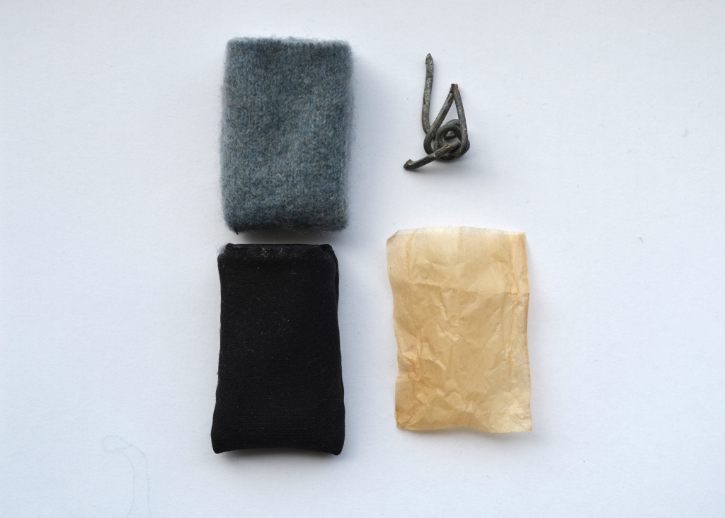 Small piece of barbed wire next to three pouches, made from different materials.